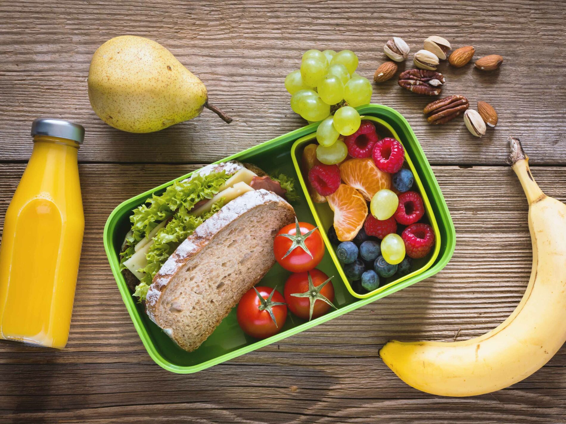Snack box with orange juice, sandwich, banana, grapes, nuts pear