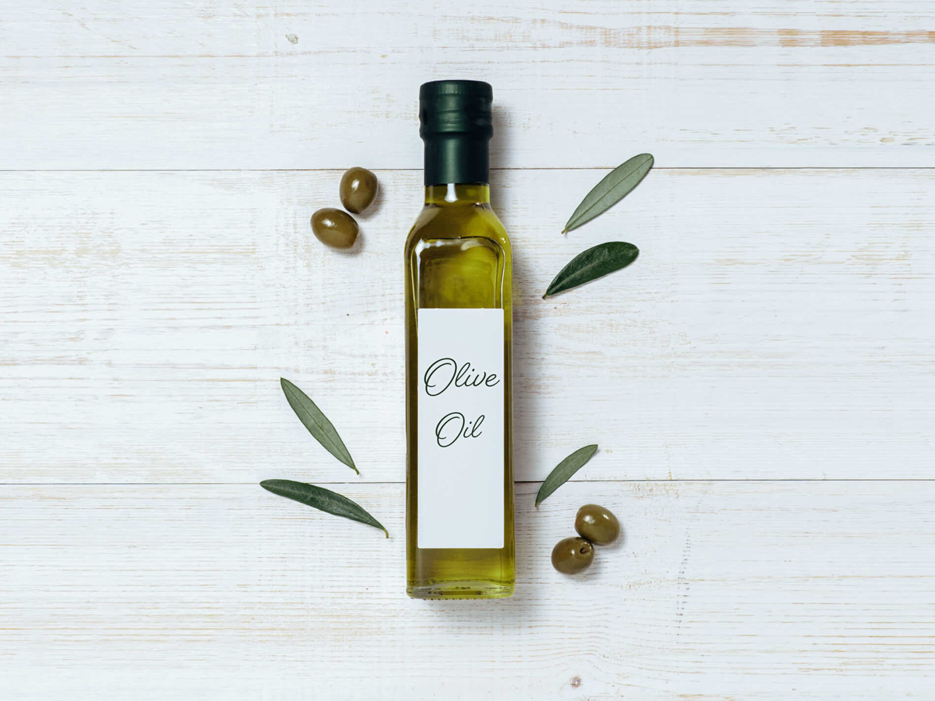 A bottle of olive oil with olive leaves and olives on white background